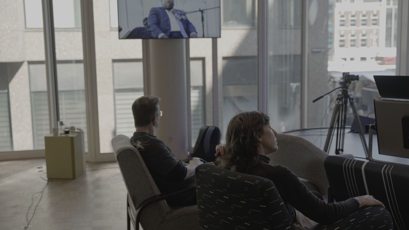 Twee mensen kijken in de zaal mee naar het gesprek op een groot scherm